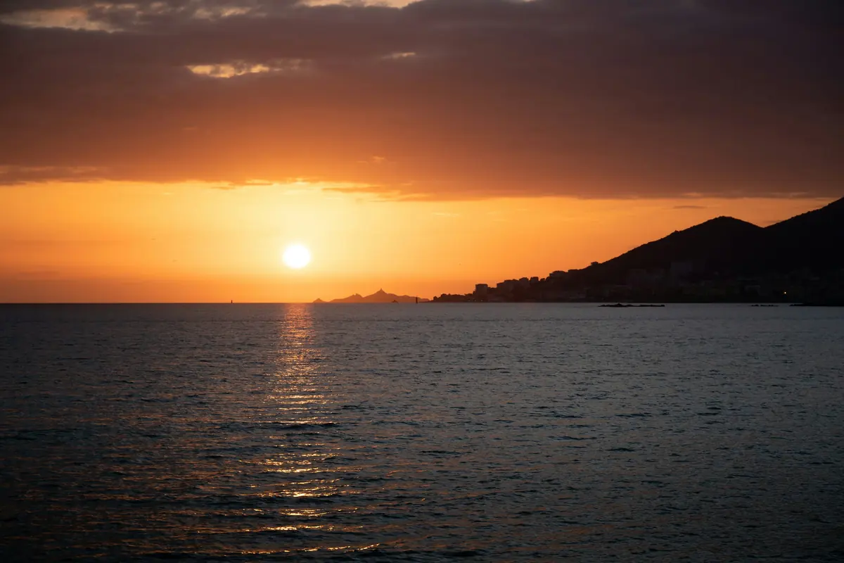 Soleil bas sur la mer, derrière une ligne de collines