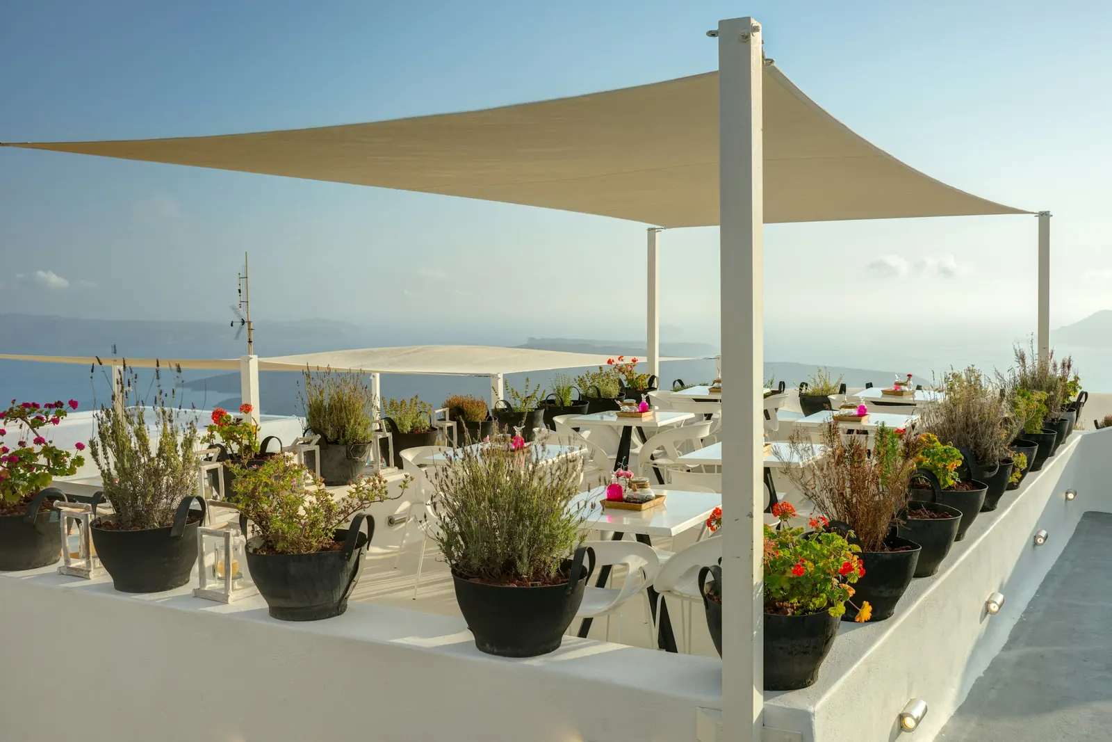 Terrasse ombragée par une toile, tables et plantes face à la mer